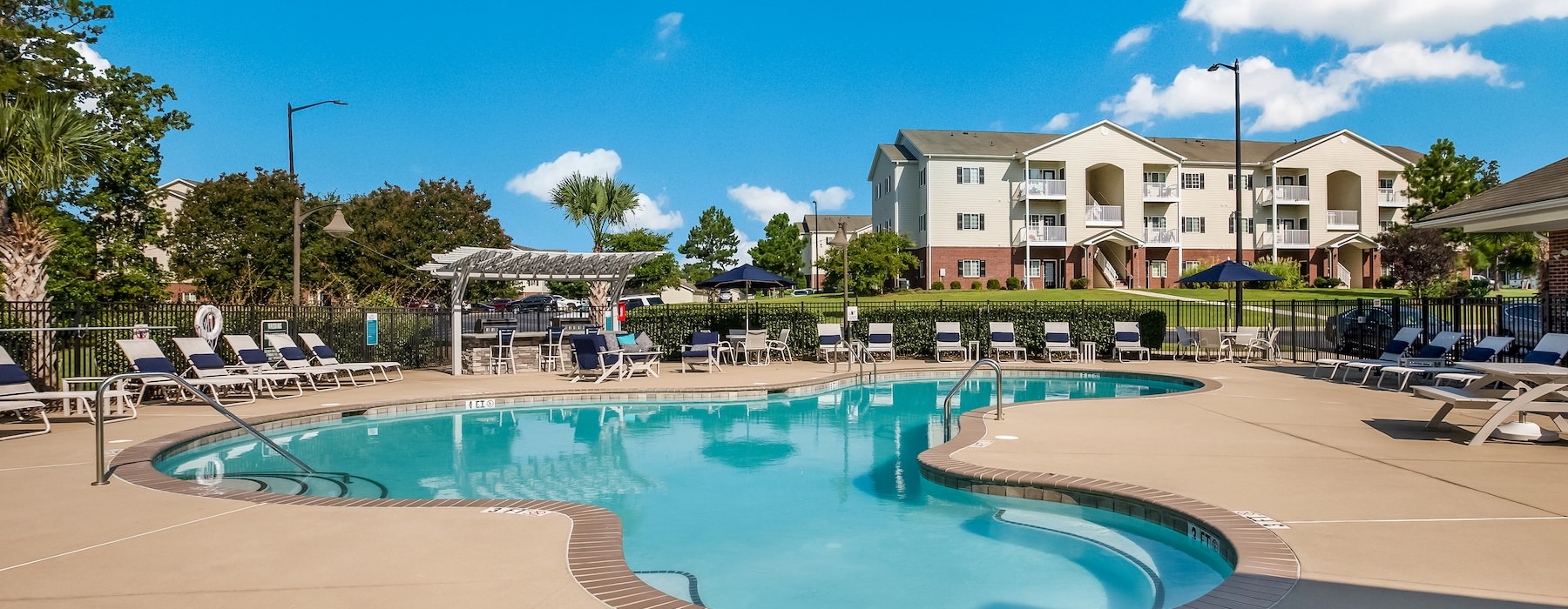 A pool in a courtyard with lounge chairs and umbrellas at The Summit on 401 apartments in Fayetteville, NC.	